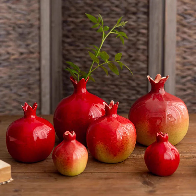 Set of red ceramic pomegranate-shaped vases on a wooden surface with a textured wall background.