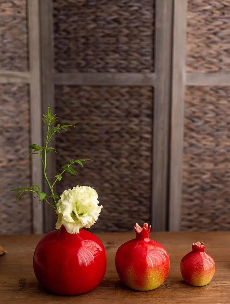 Decorative vases with flowers and pomegranates on a wooden surface with a textured wall background.