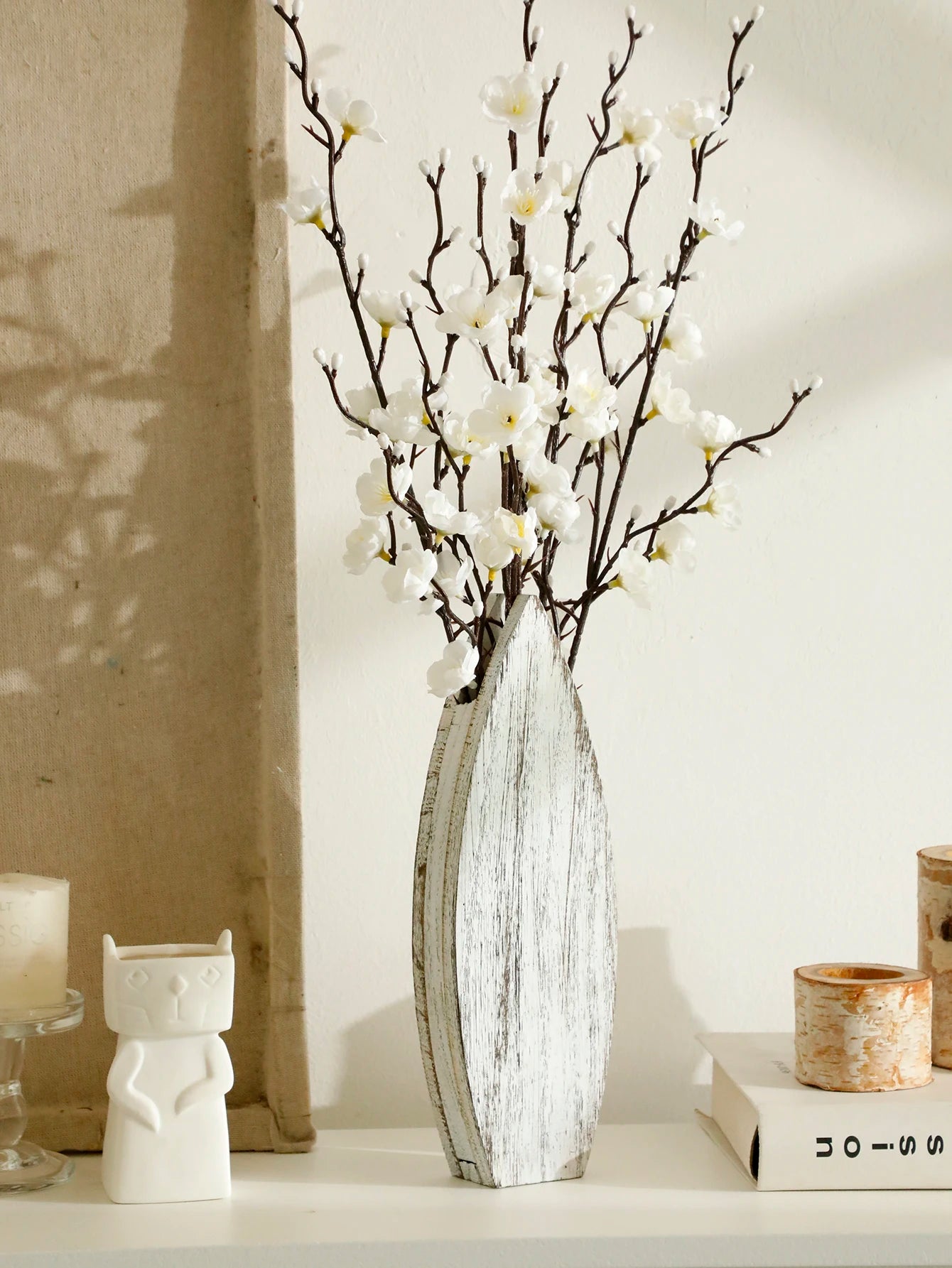White surfboard-shaped wooden vase with rustic distressed finish, styled with white blossom branches for relaxed coastal home decor.