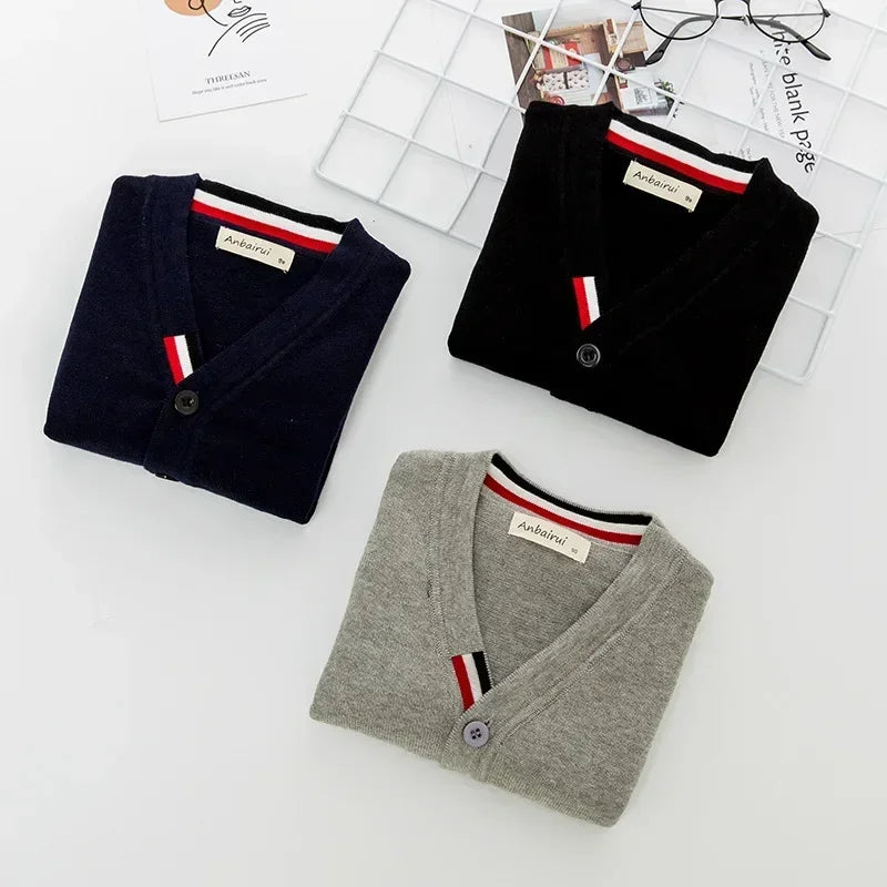 Three folded cardigans in black, gray, and navy on a white surface with a magazine underneath.