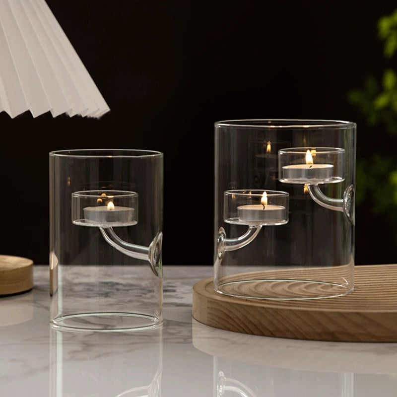 Two clear glass candle holders with candles on a reflective surface.
