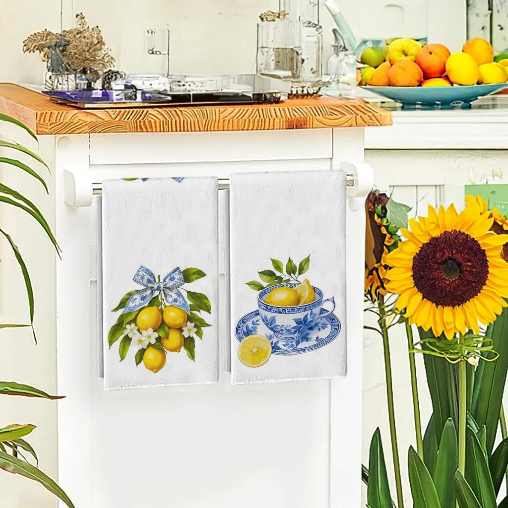 Decorative kitchen towels with lemon and teacup designs hanging on a cabinet door, surrounded by fruits and flowers.