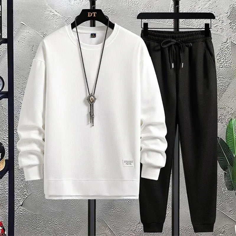 White hoodie and black pants on hangers against a gray wall.