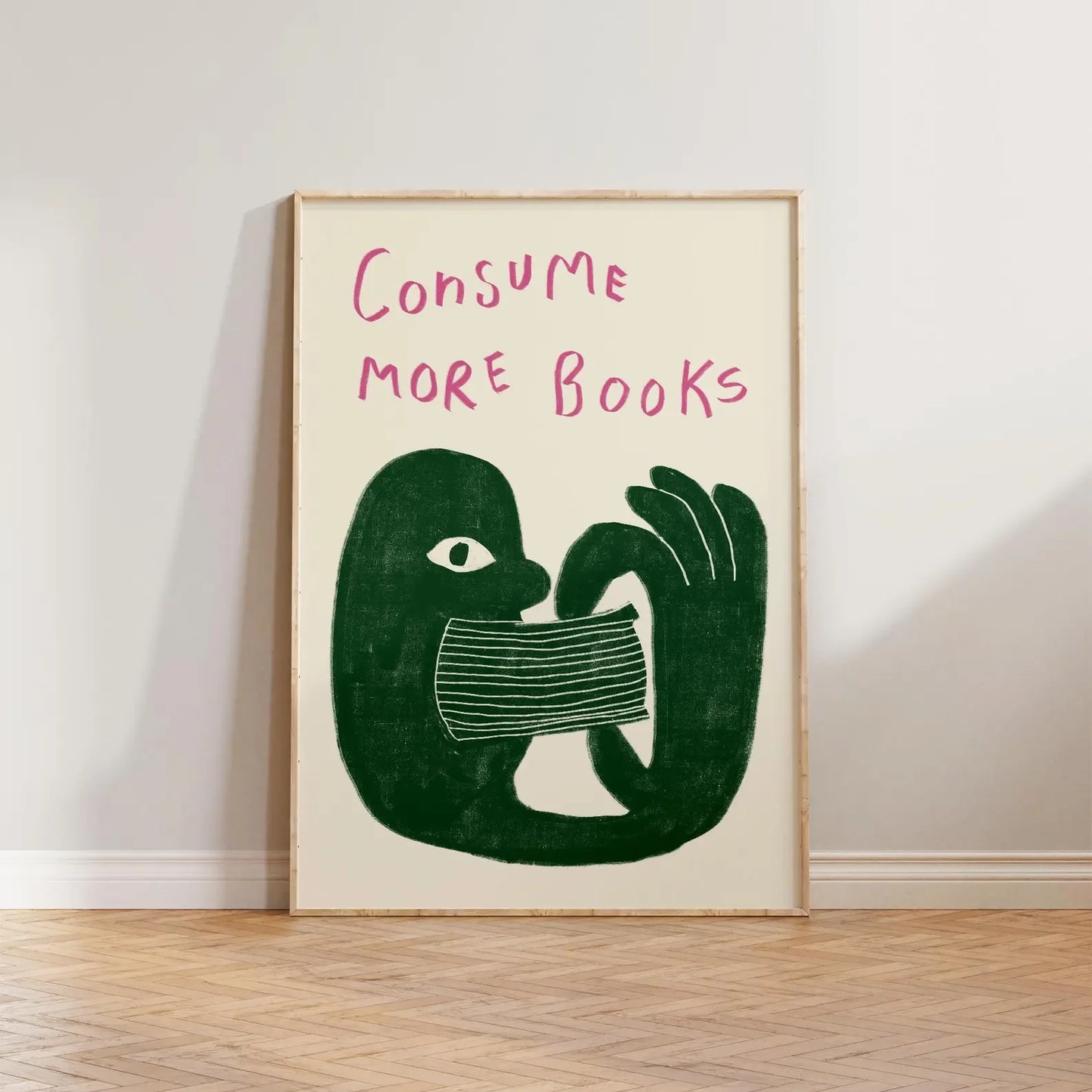 Framed artwork with a green abstract figure and pink text 'Consume More Books' on a white wall.