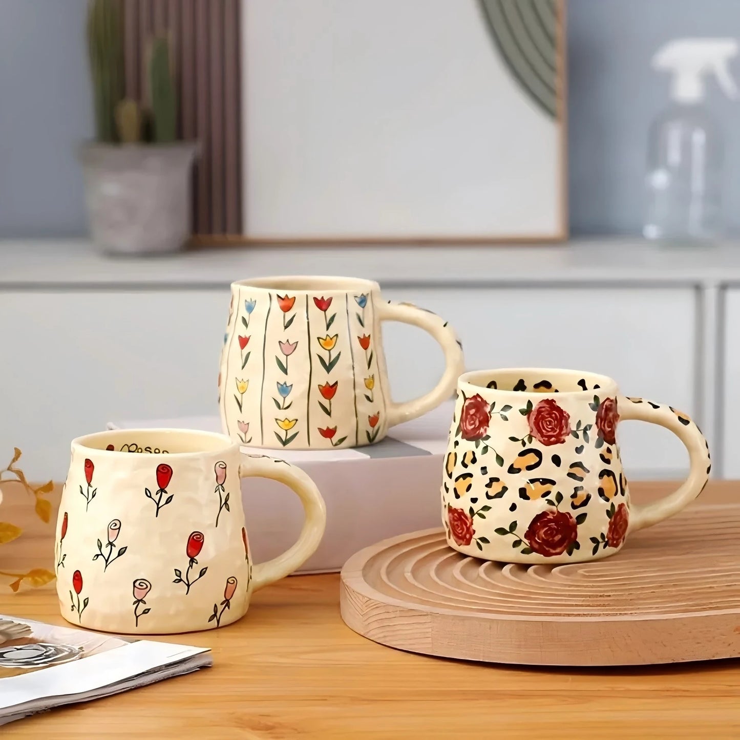 Three ceramic mugs with floral and leopard print designs on a wooden surface.