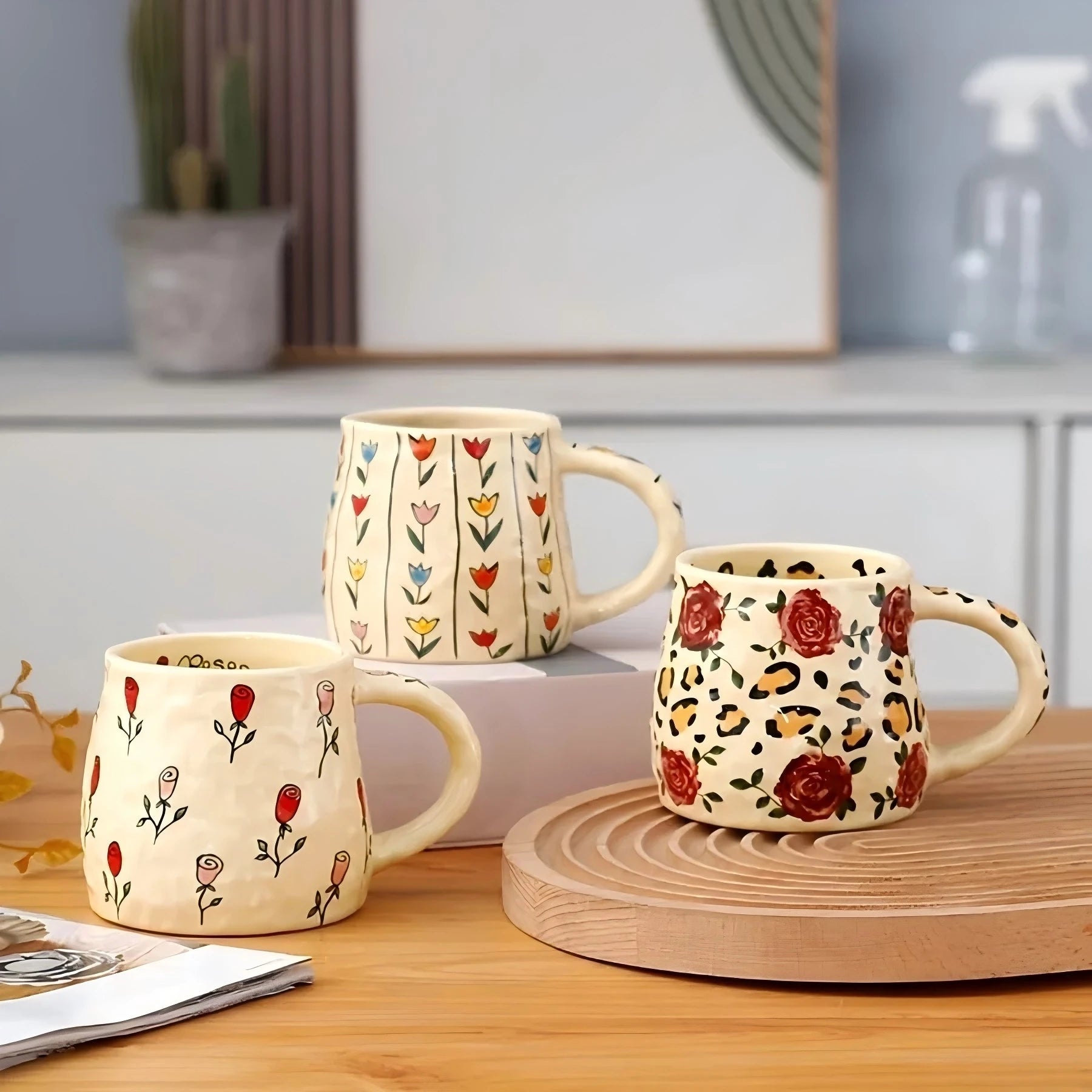 Three ceramic mugs with floral and leopard print designs on a wooden surface.