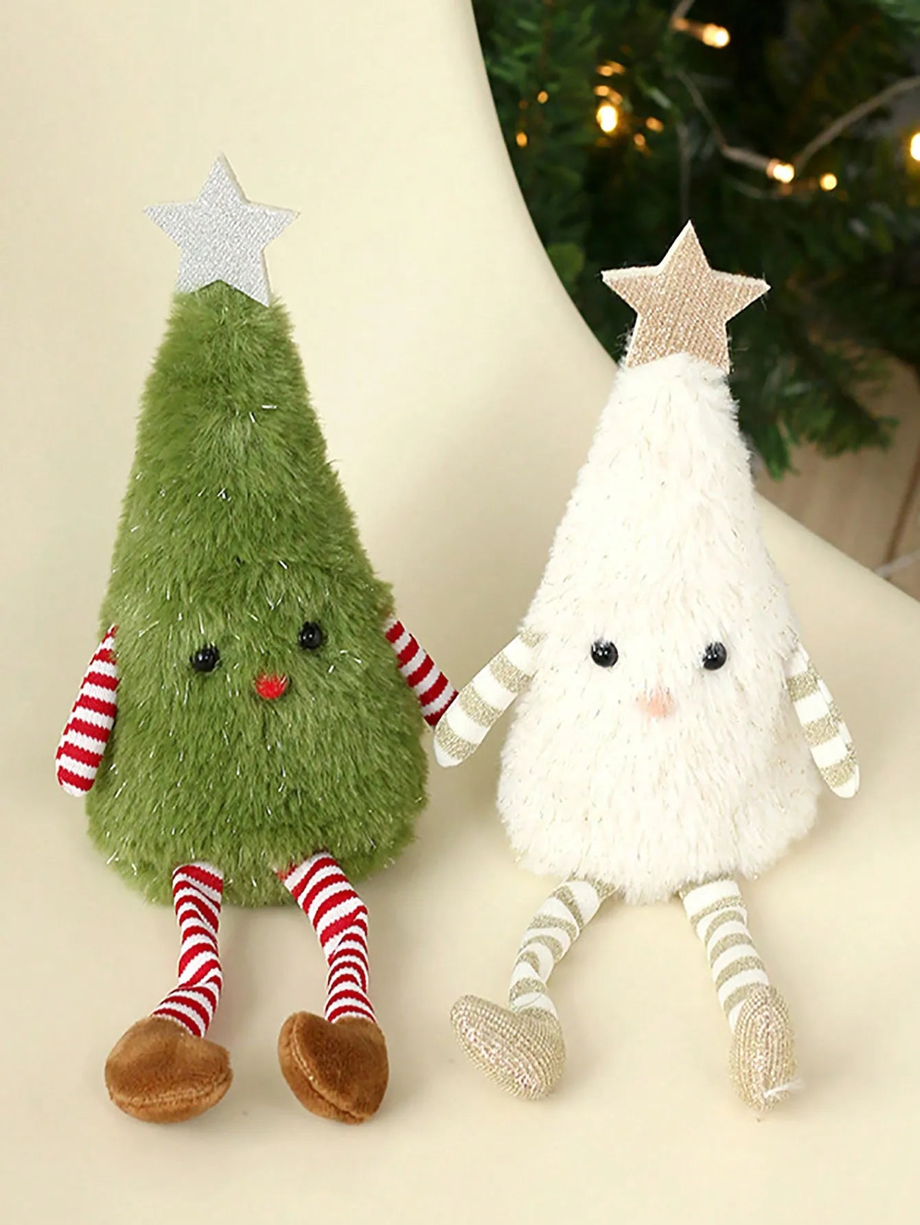 Two plush Christmas tree decorations, one green and one white, with star toppers on a neutral background.