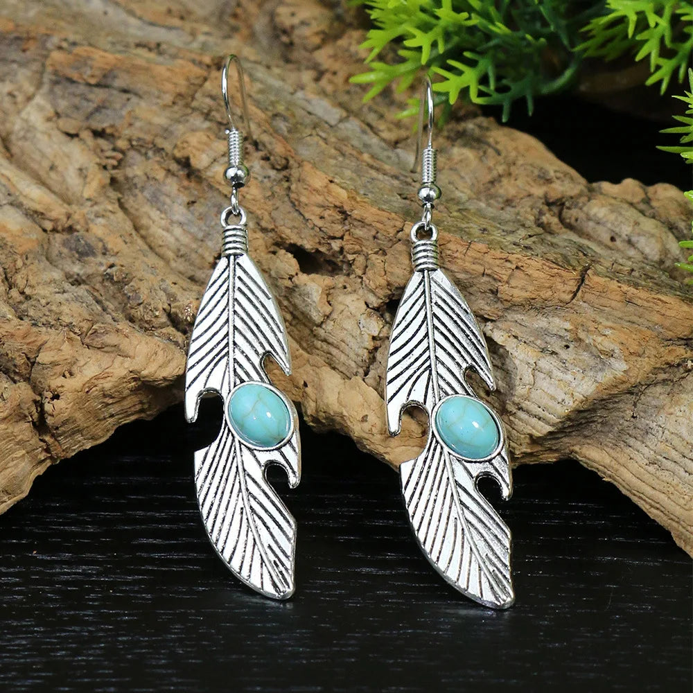Silver feather-shaped earrings with turquoise stones on a wooden surface.