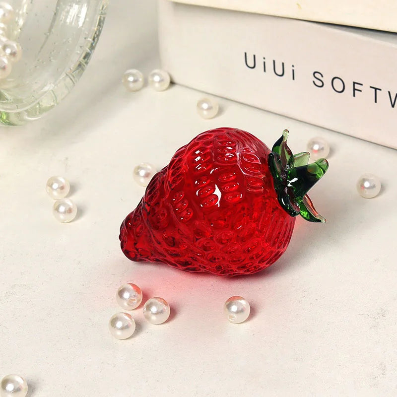 Red strawberry-shaped object with green stem on a light surface with pearls