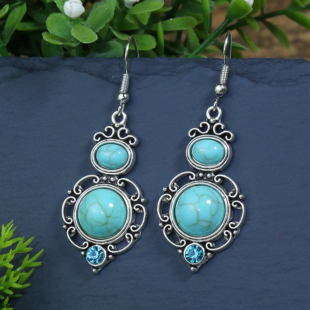 Turquoise stone earrings with silver detailing on a dark surface with greenery.