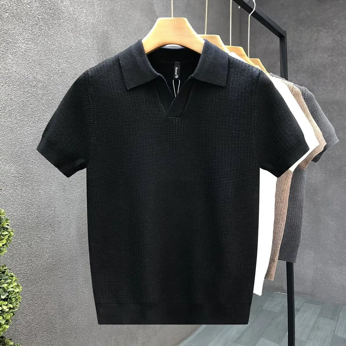 Black polo shirt on a hanger against a gray wall