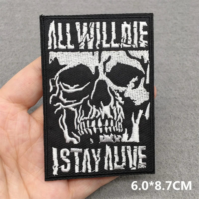Skull patch with 'All Will Die, I Stay Alive' text held in a hand against a gray background