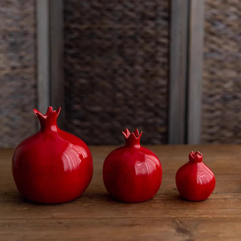 Three red ceramic pomegranate-shaped vases on a wooden surface with a stone wall background.
