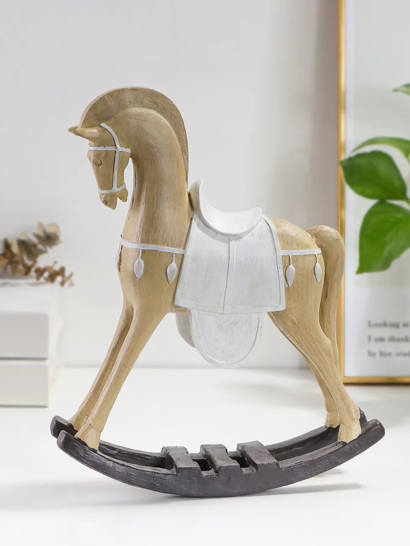 Wooden rocking horse on a white surface with a plant in the background