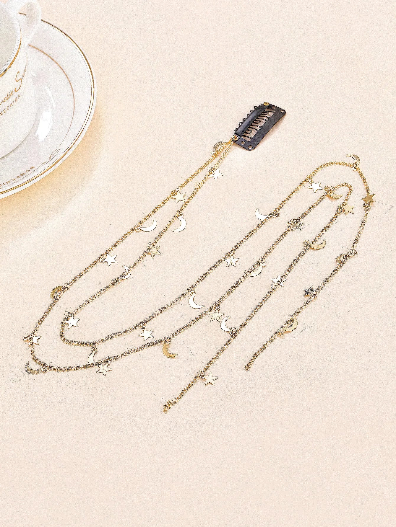 Gold chain necklace with star and moon charms on a beige surface.