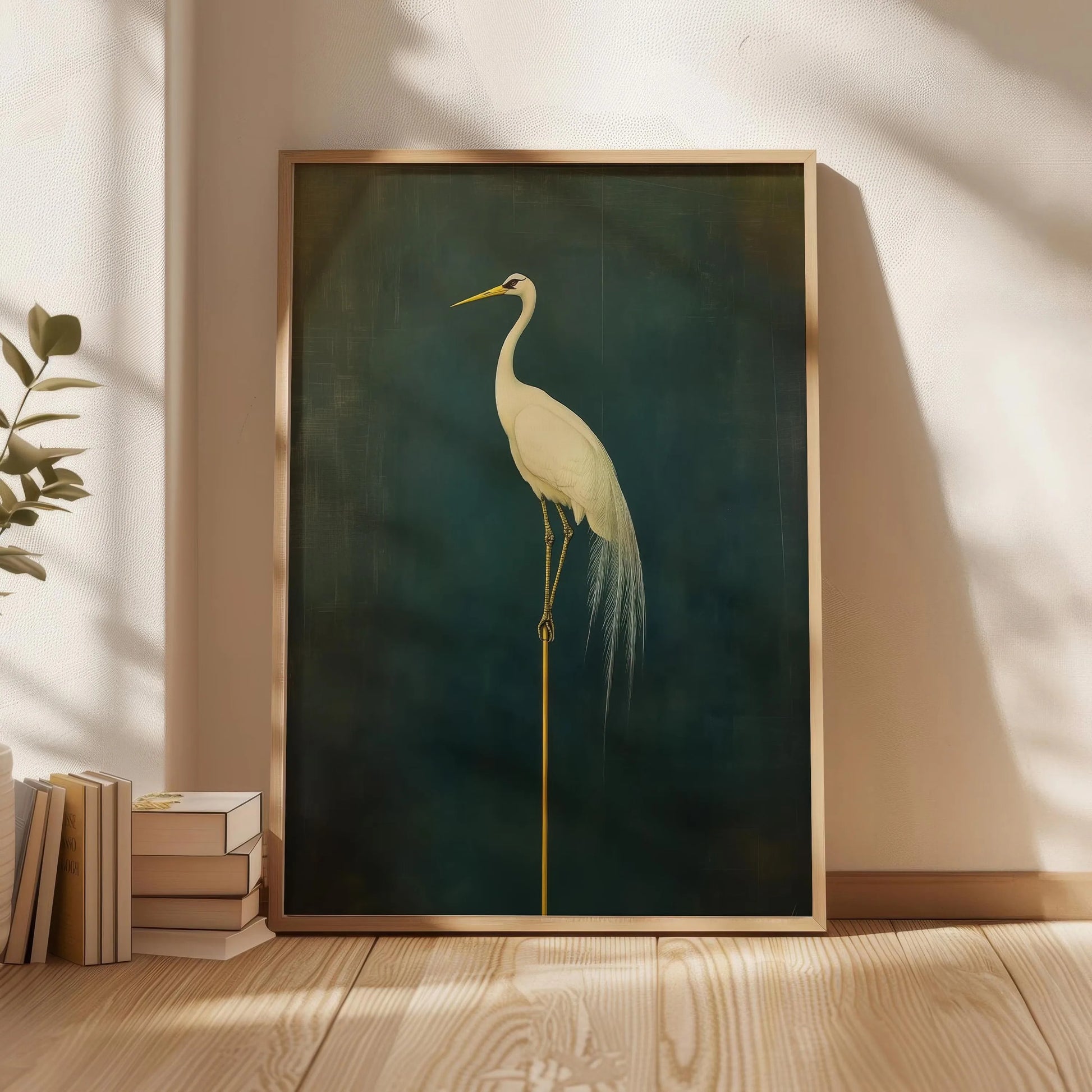 Framed artwork of a crane on a dark green background, leaning against a wall with natural light casting shadows.