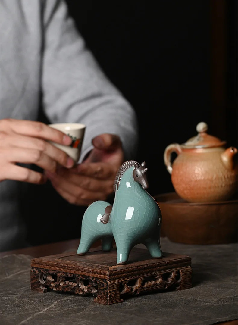 Tea ceremony setup with a ceramic horse figure on a wooden stand, a teacup, and teapot.