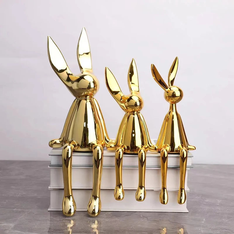 Three gold rabbit sculptures on a stack of books with a light purple background