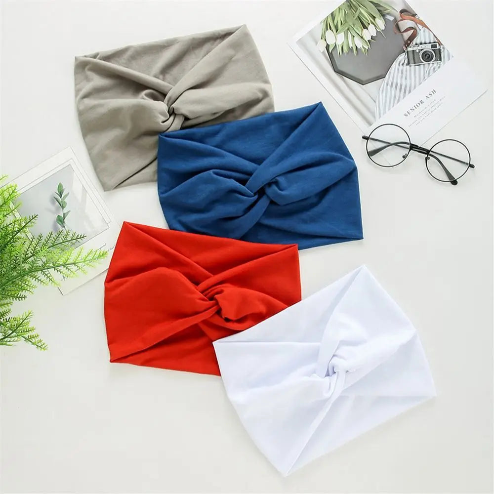 Four headbands in gray, blue, red, and white on a light surface with glasses and plants.