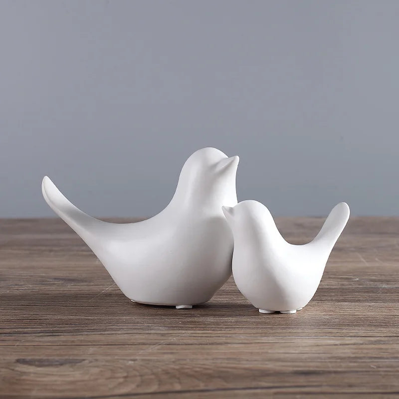 Two white ceramic birds on a wooden surface with a gray background
