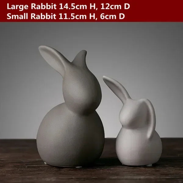Two ceramic rabbit figurines, one large and one small, on a wooden surface with a gray background.