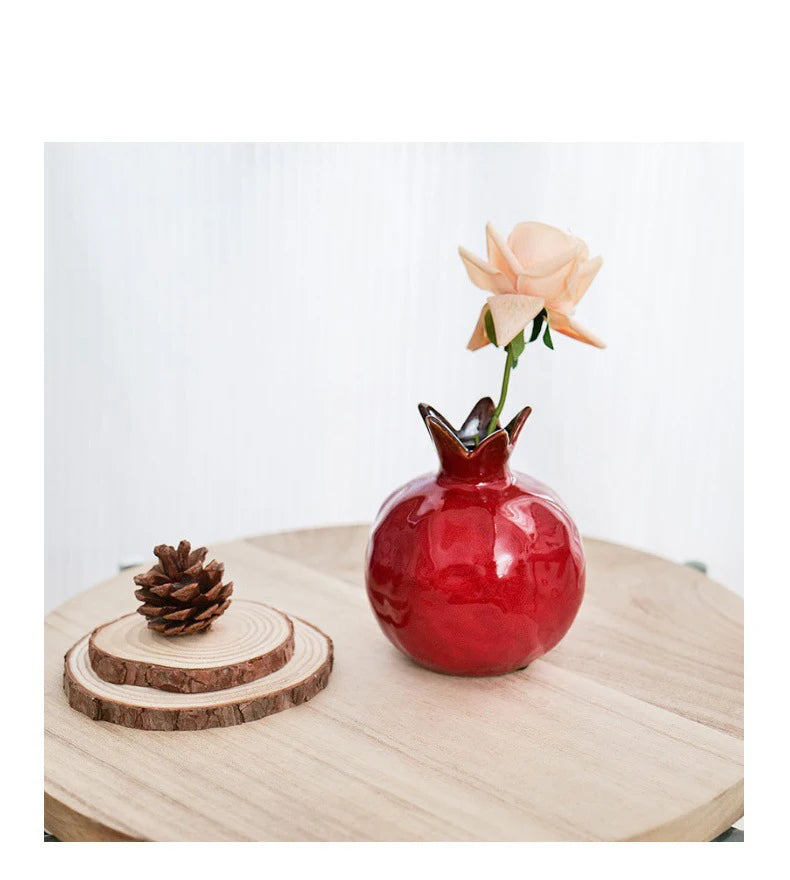 Red pomegranate vase with a flower on a wooden surface