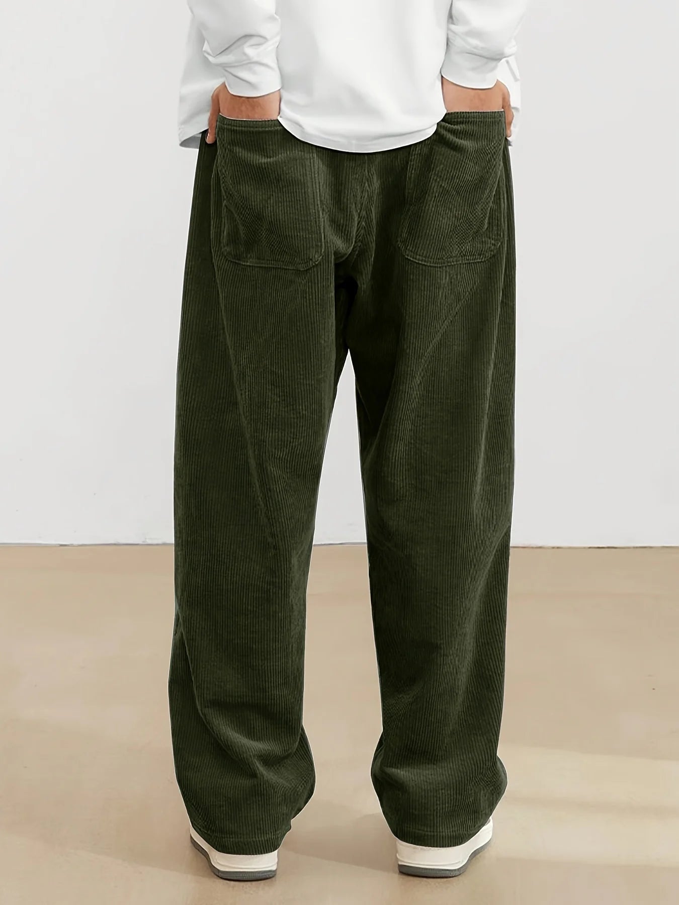 Person wearing green corduroy pants and a white shirt on a plain background