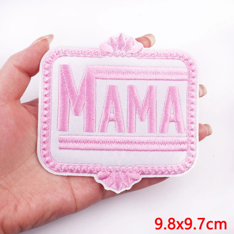 Pink 'MAMA' patch held in a hand with a white background