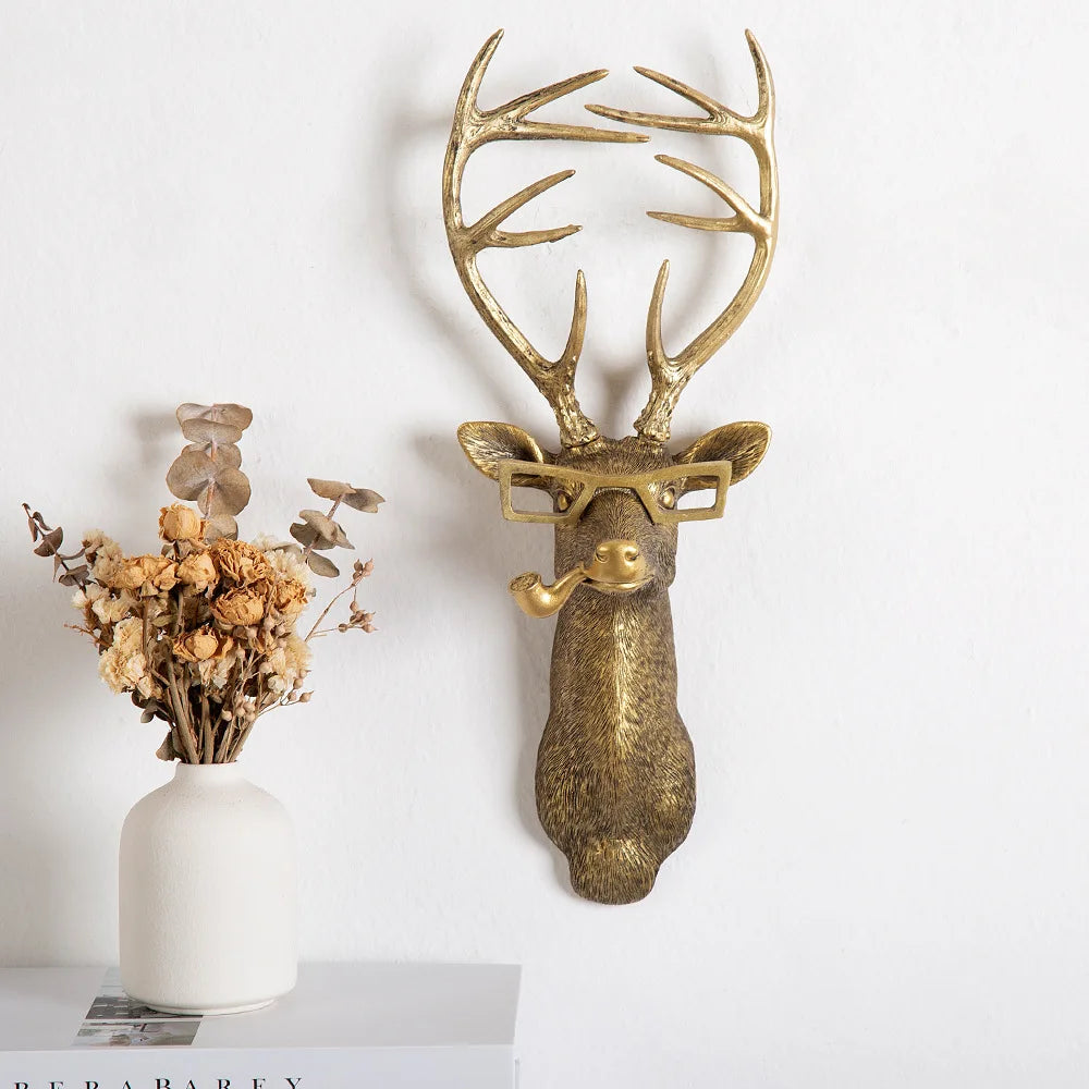Decorative gold deer head with antlers on a white wall, next to a vase with dried flowers.