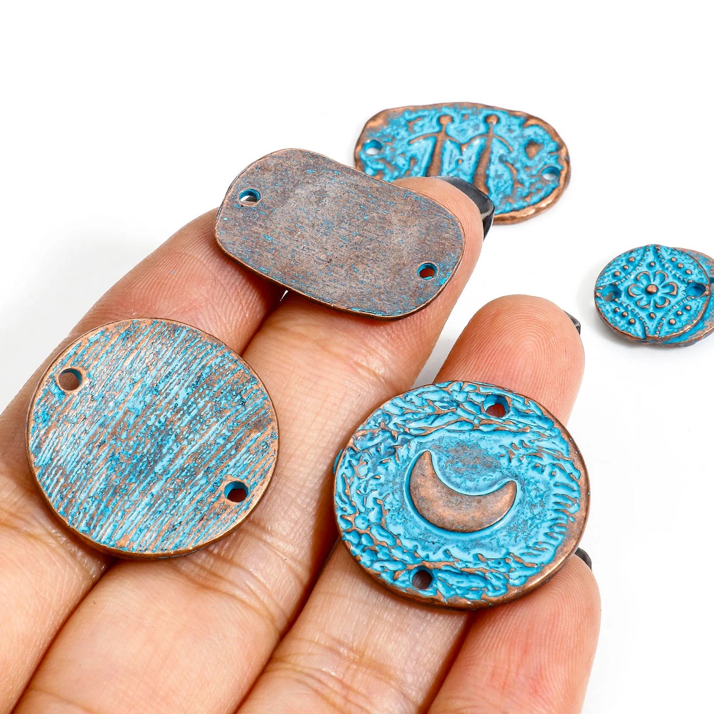 Hand holding blue and bronze metal pendants with intricate designs on a white background