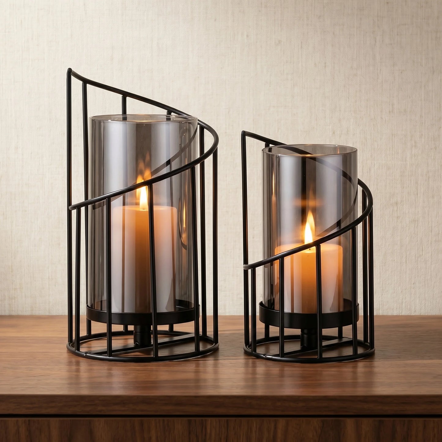 Set of two modern black spiral glass candle holders with smoked hurricane glass displayed on a wooden table in a contemporary home interior.