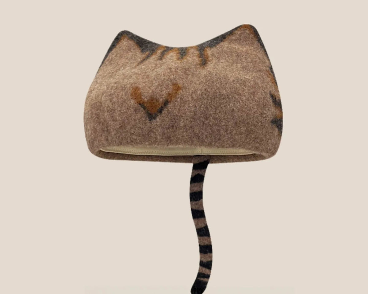 A wool cat-shaped hat in taupe-brown with dark stripes on the tail, shown on a plain beige background