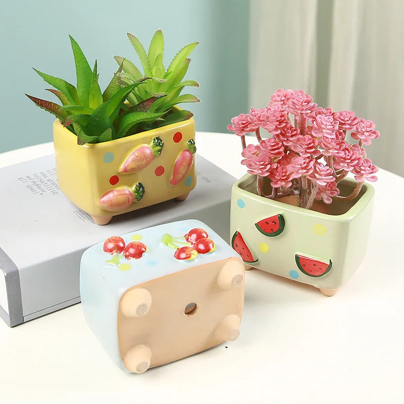 Three colorful ceramic planters with plants on a light surface.