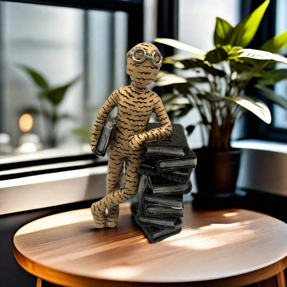 Decorative figure of a person in a suit with goggles holding books on a wooden surface.