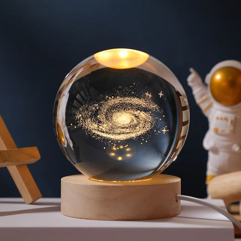 Glass sphere with galaxy design on a wooden base, next to an astronaut figurine.