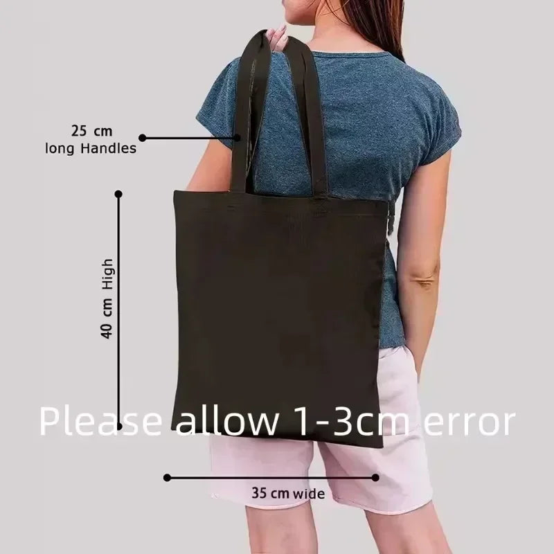 Black tote bag held by a person with measurements indicated on a gray background
