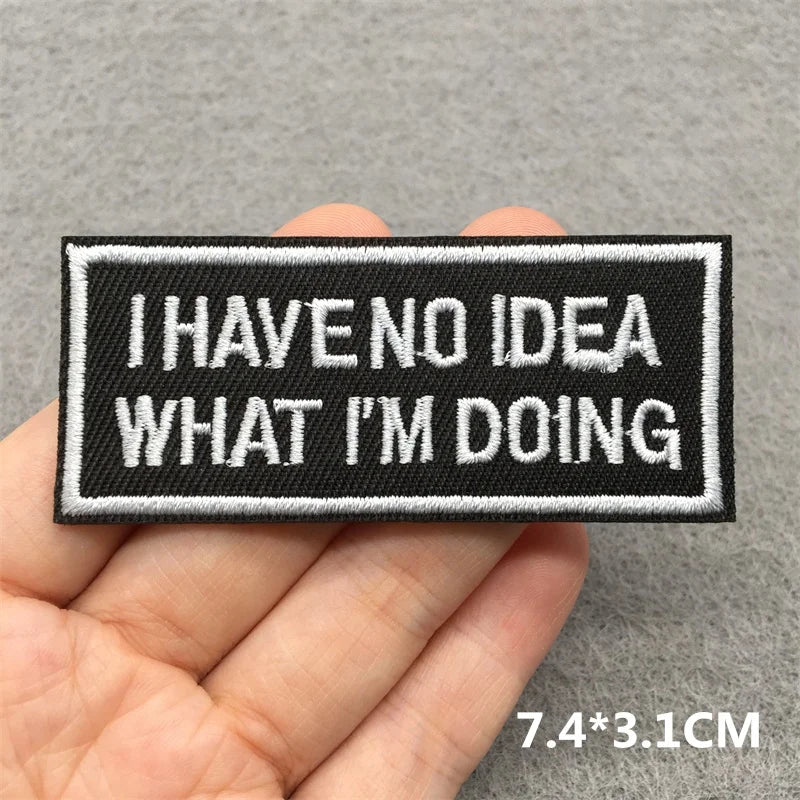 Embroidered patch with text 'I HAVE NO IDEA WHAT I'M DOING' held in a hand against a gray background.