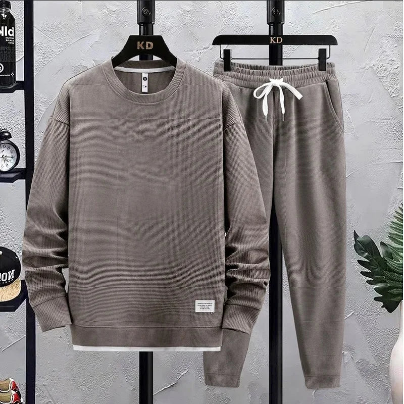 Gray sweatshirt and pants set on hangers against a gray wall.