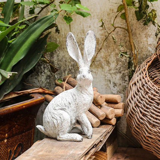 Decorative rabbit statue on a wooden surface with plants and logs in the background