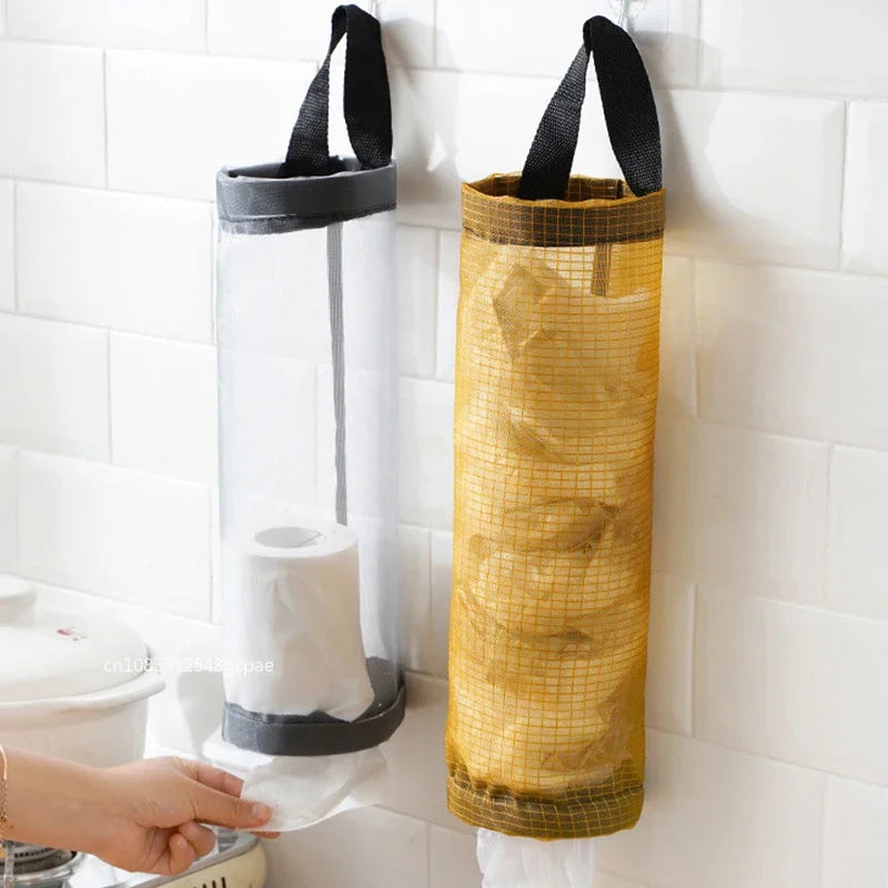 Hand reaching for toilet paper in a transparent holder with a yellow mesh bag on a tiled bathroom wall.