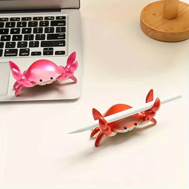 Two crab-shaped desk organizers, one pink and one red, on a desk with a laptop.