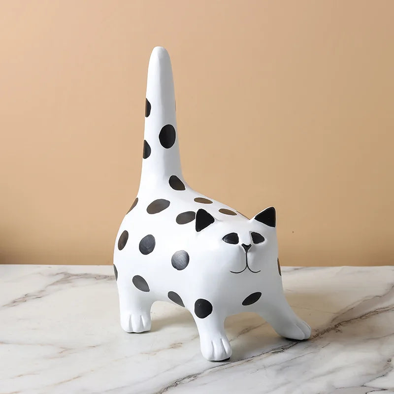 White ceramic cat figurine with black spots on a marble surface against a beige background