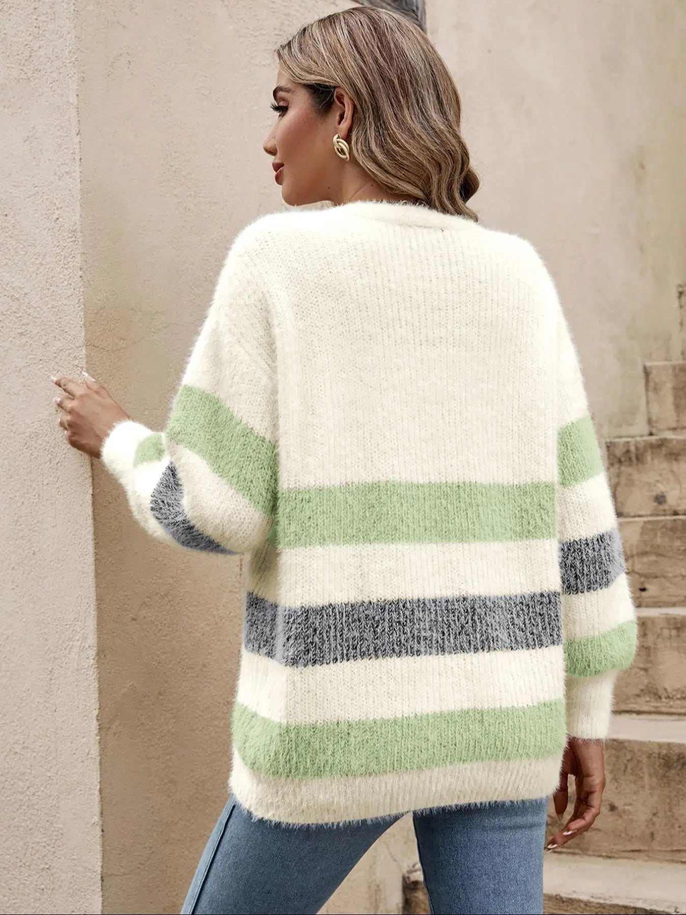 Woman wearing a striped sweater with green and gray stripes, standing against a beige wall.