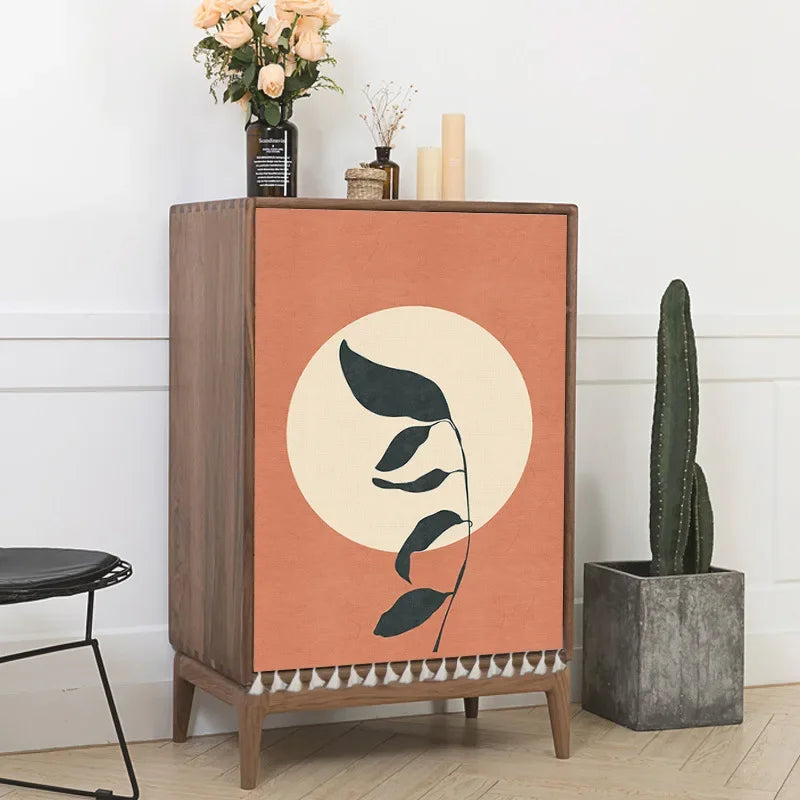 Wooden cabinet with decorative leaf design on a peach background, placed in a room with a white wall and a plant.