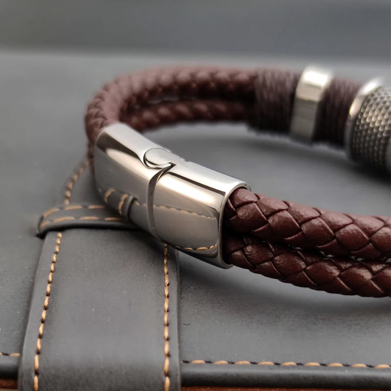 Brown braided leather bracelet with silver clasp on a textured surface