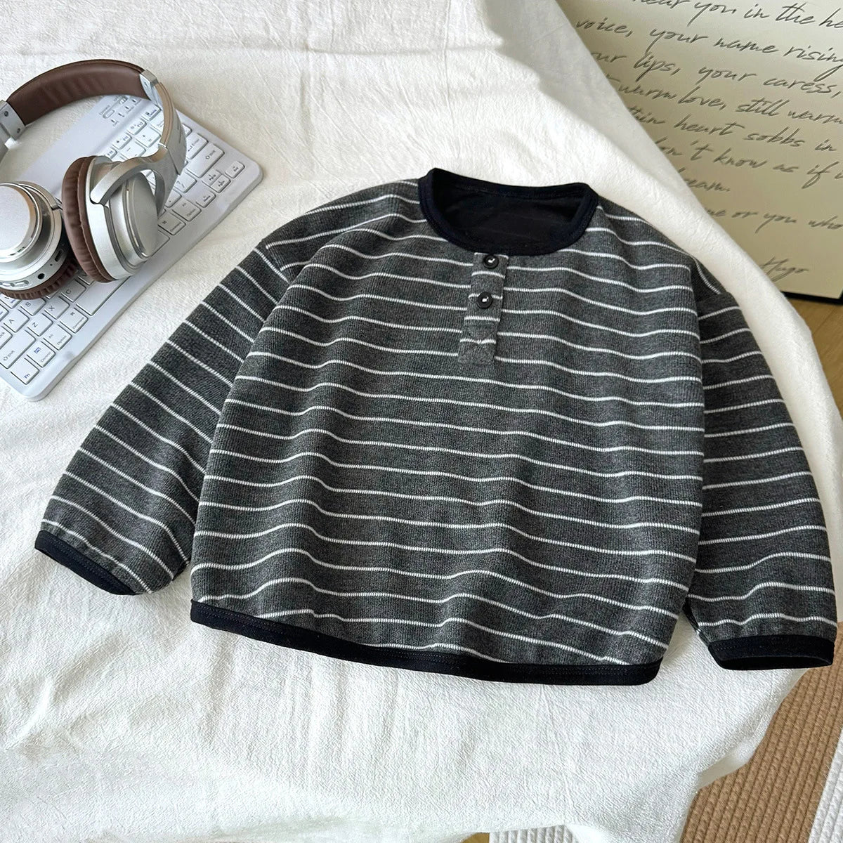Striped sweater on a white surface with headphones and a book in the background