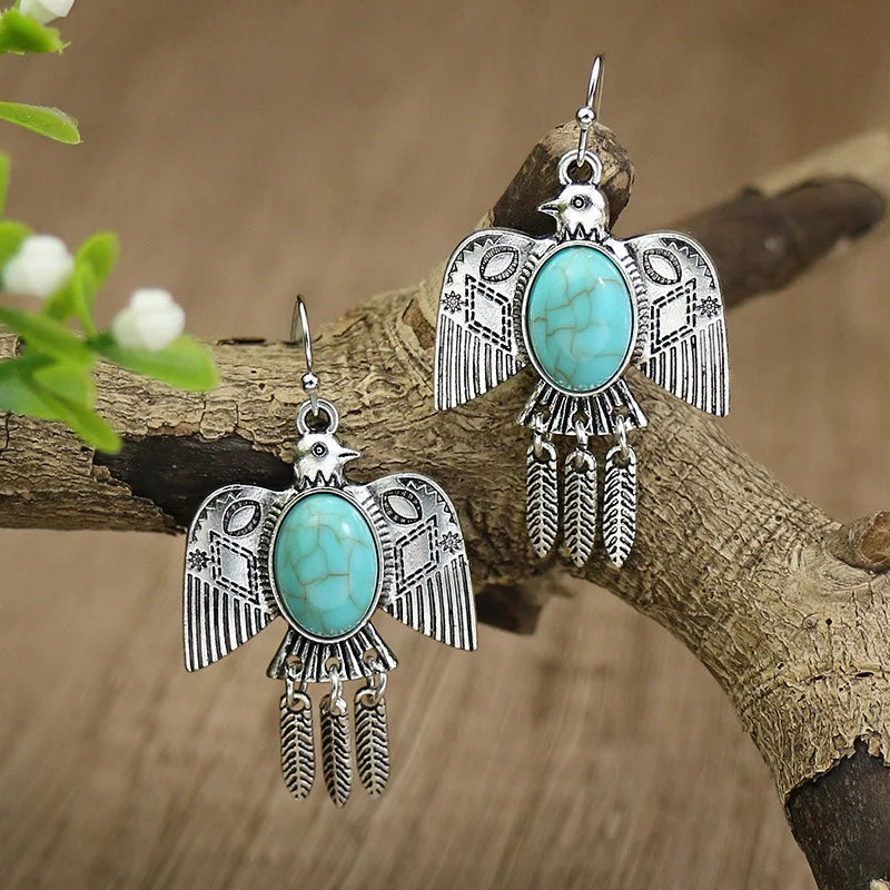 Pair of silver and turquoise bird-shaped earrings on a branch with a natural background