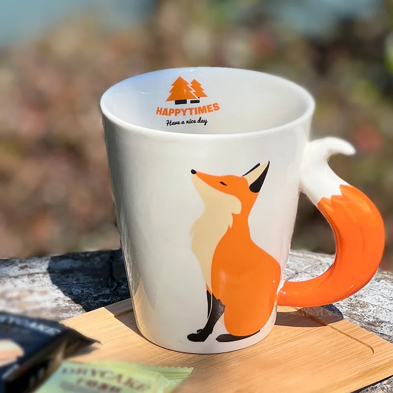 White mug with fox design and 'Happy Times' logo on a wooden surface with blurred natural background