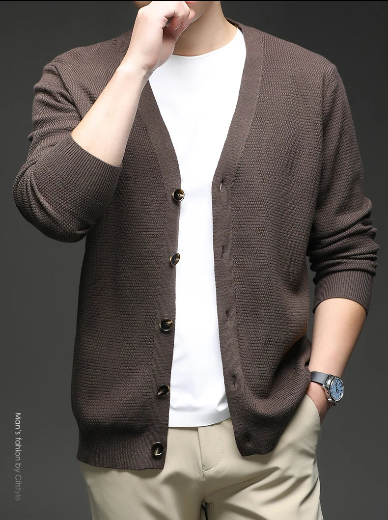Person wearing a brown cardigan over a white shirt with a gray background