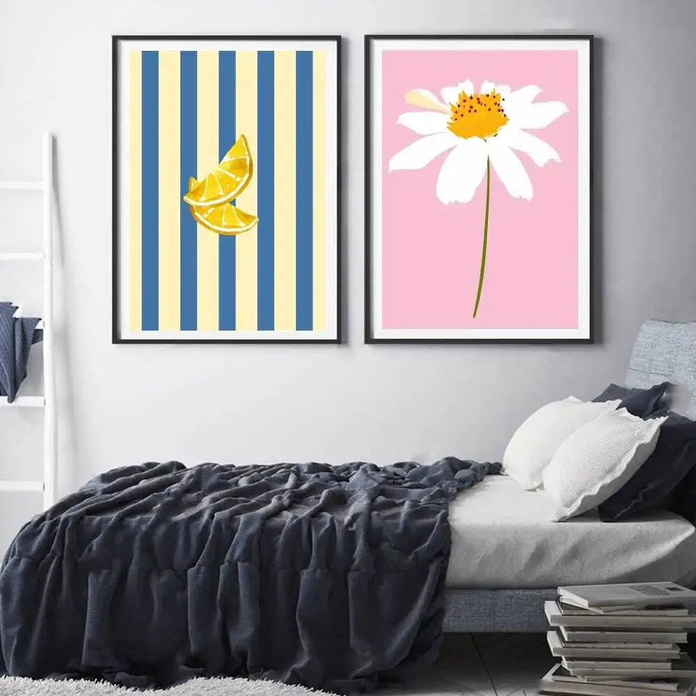 Two framed artworks on a wall above a bed, one with striped design and lemon slices, the other with a daisy flower.